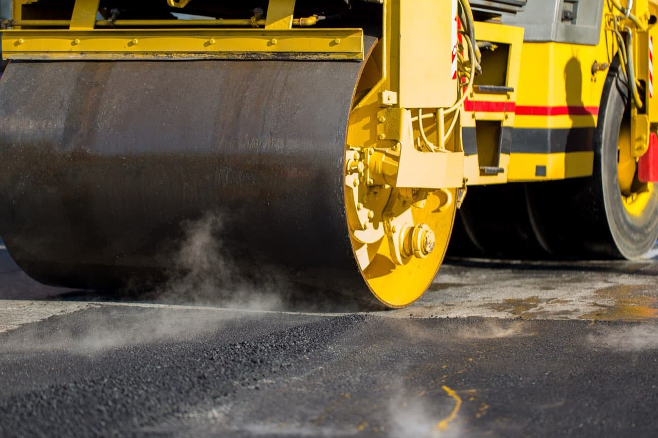 Yellow road roller compacting fresh, steaming asphalt