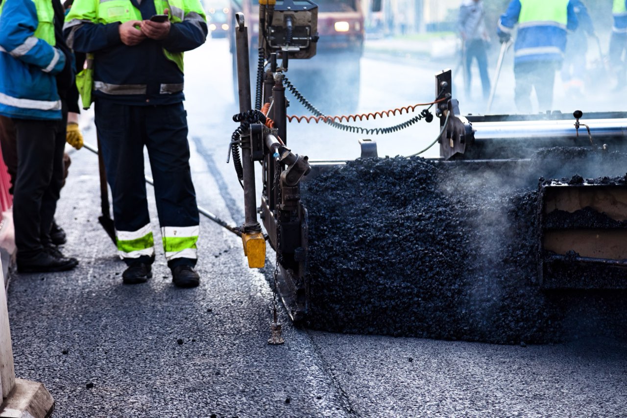 Construction crew paving a city street with a yellow paver machine